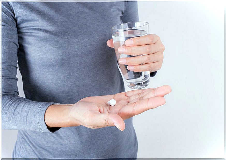 Woman with a pill in one hand and a glass of water in the other